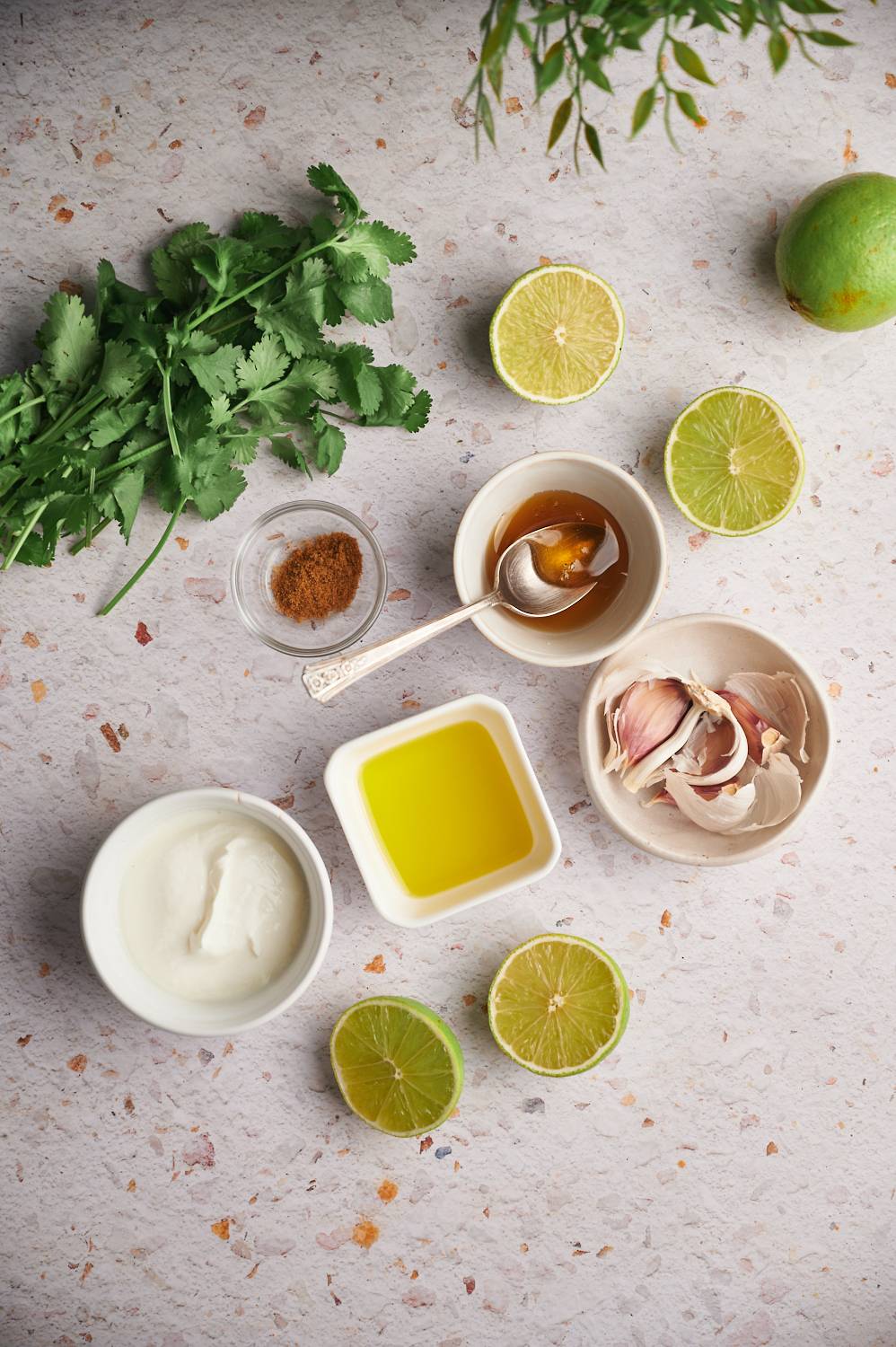 Ingredients for cilantro lime sauce including fresh cilantro, fresh limes, olive oil, yogurt, garlic, honey, and cumin.