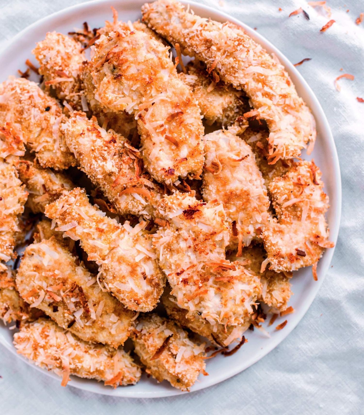 Baked coconut chicken fingers on a plate with a crispy shredded coconut and Panko coating.