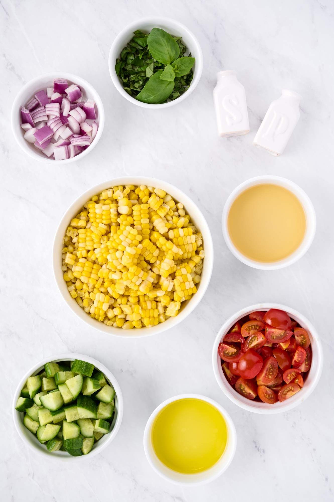 Ingredients for corn salad including fresh corn, tomatoes, cucumbers, basil, and dressing.