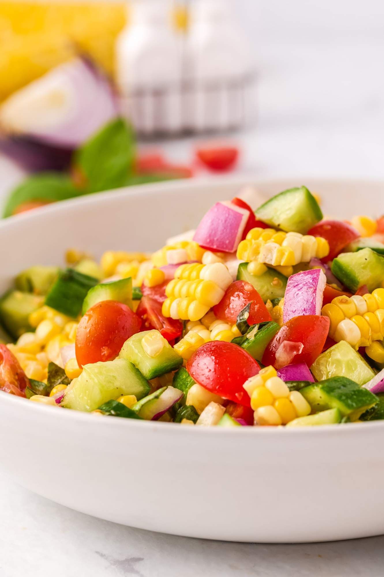 Fresh salad with corn, tomatoes, red onions, and cucumbers tossed with vinaigrette and basil.