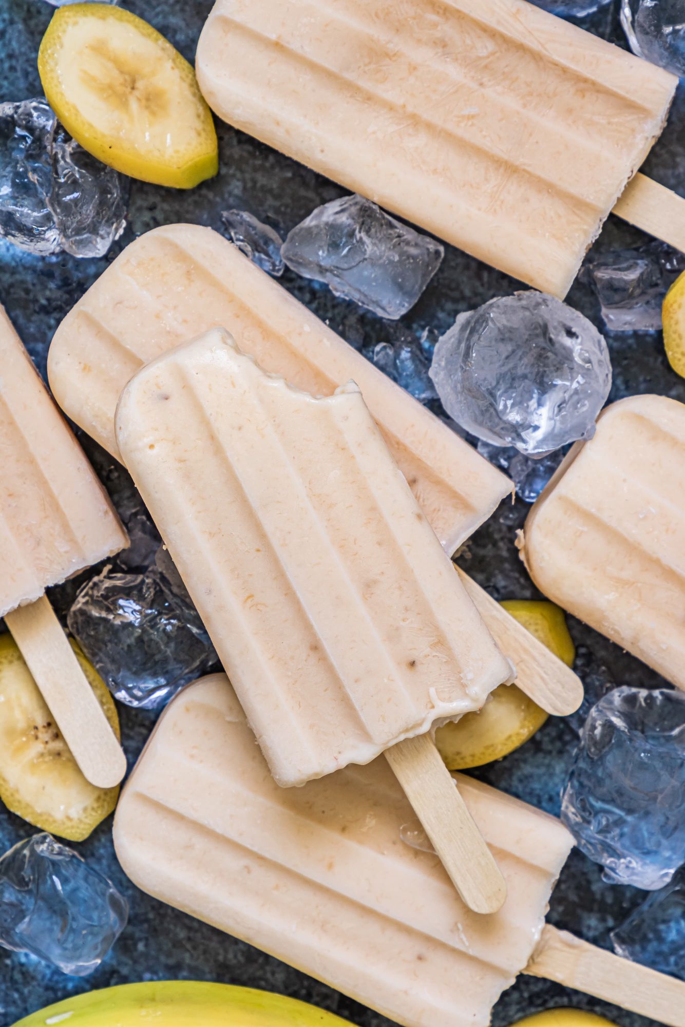 Homemade banana popsicles made with fresh bananas on a tray with ice and banana slices.