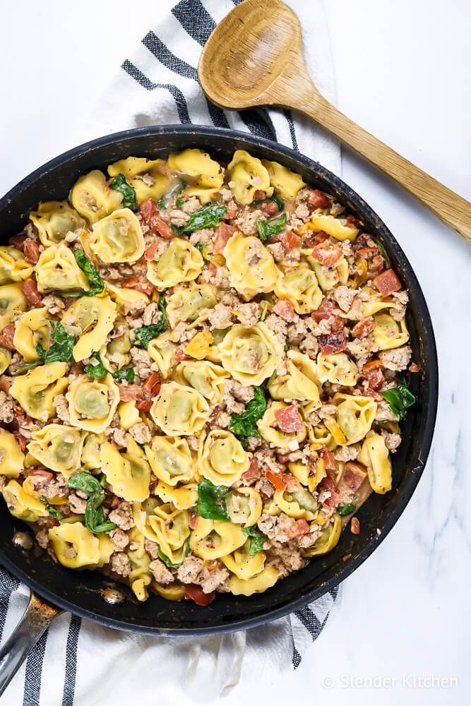 Chicken tortellini with creamy tomato sauce in a black skillet with a napkin and wooden spoon.