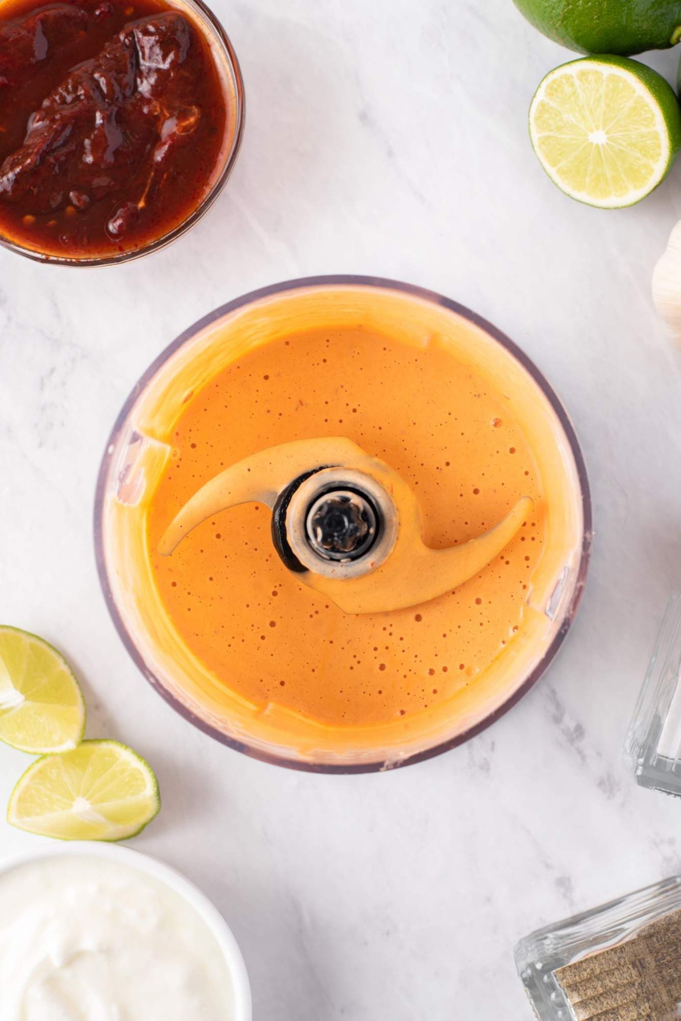 Homemade chipotle sauce in a food processor with chipotle peppers and limes on the side.