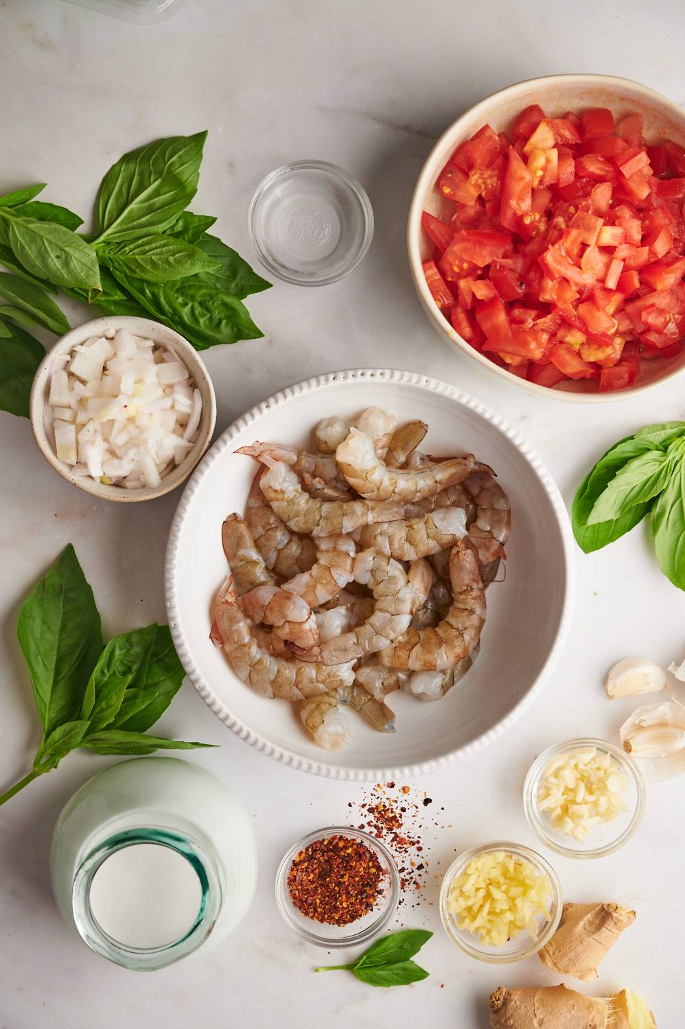 Ingredients for creamy coconut shrimp including raw shrimp, tomatoes, coconut milk, ginger, garlic, red pepper flakes, and basil leaves.