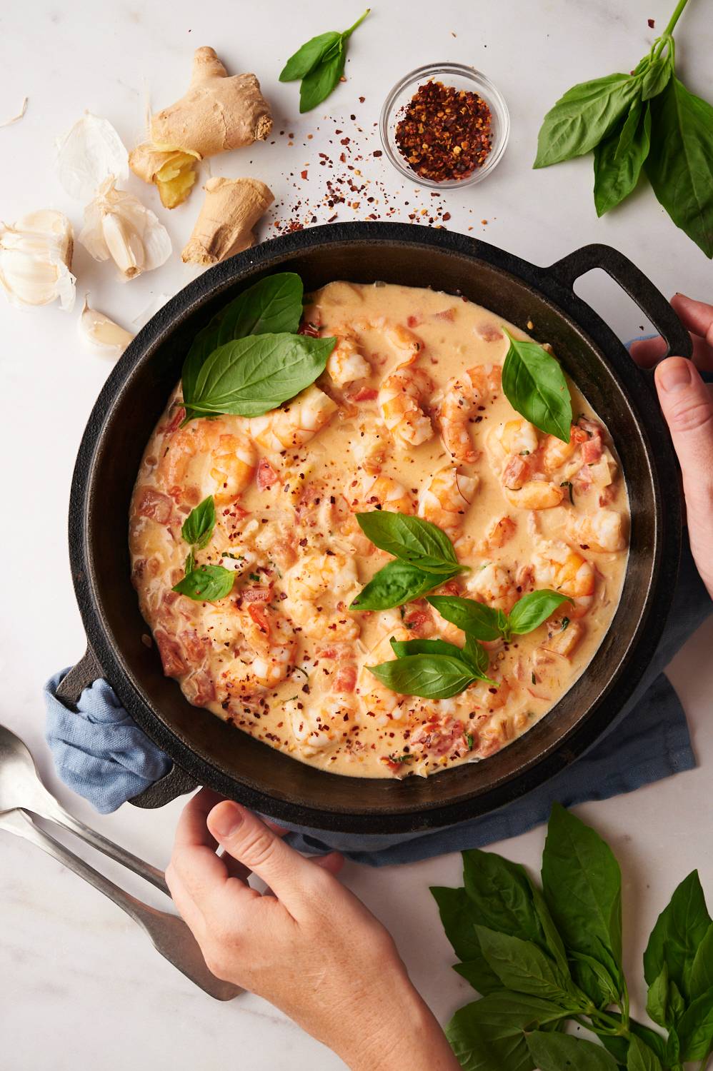 Coconut milk shrimp with tomatoes, red pepper flakes, and basil in a black skillet with ginger and garlic on the side.