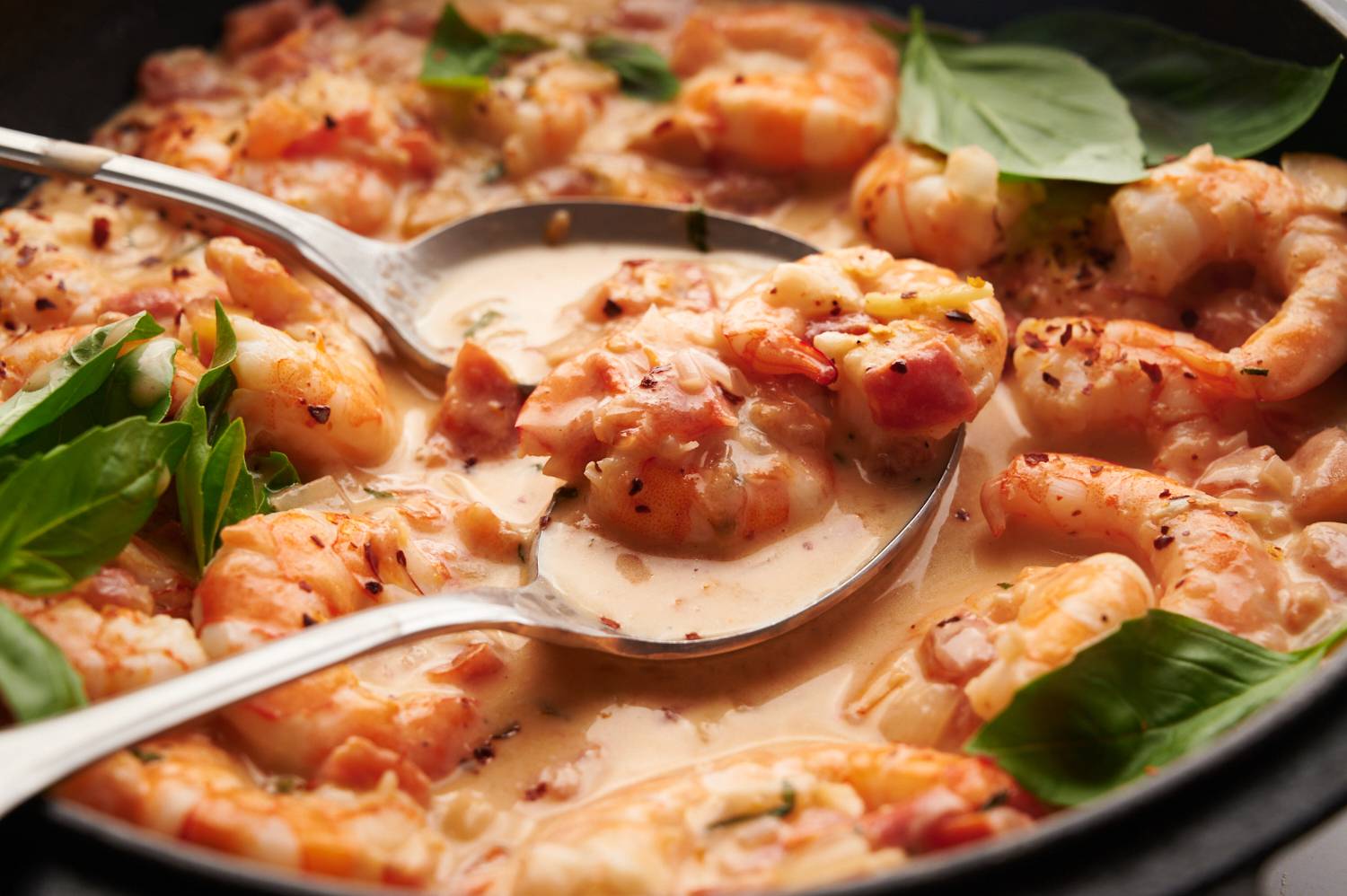 Creamy tomato coconut shrimp in a skillet with two spoons.