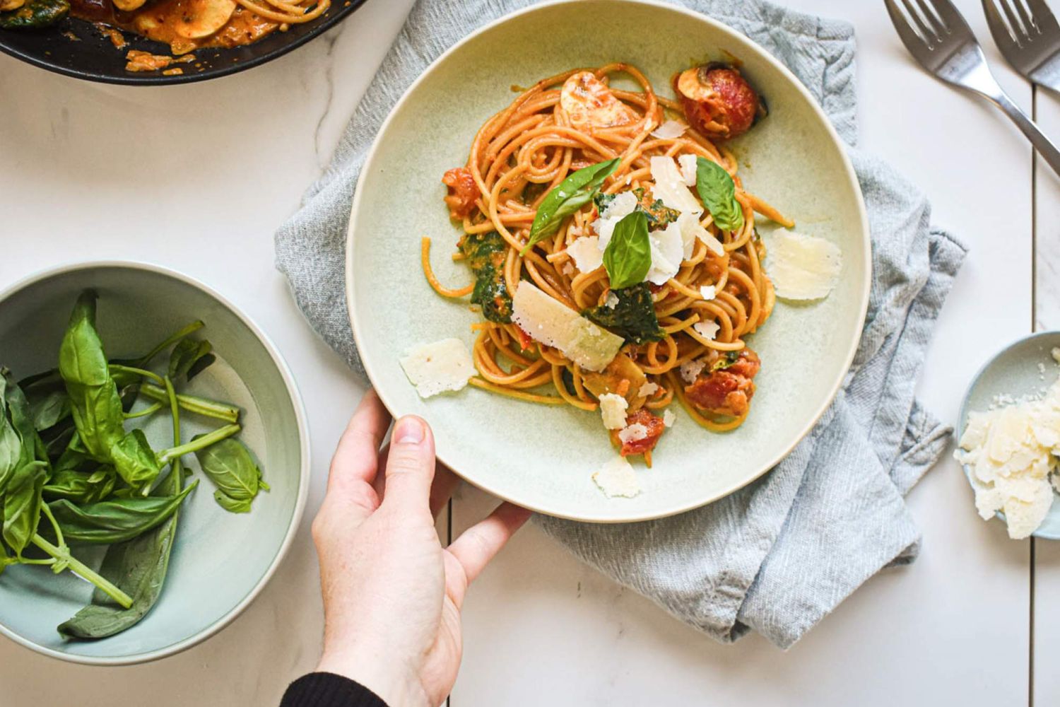 Tomato Spinach pasta with a creamy sauce and mushrooms on a plate with greens on the side.