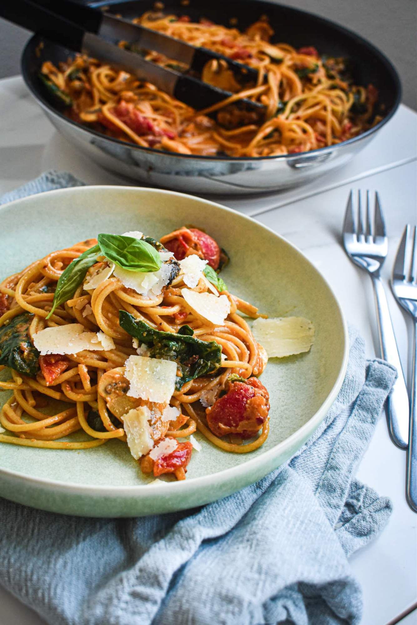 Mushroom spinach pasta with a creamy tomato sauce on a blue plate with Parmesan cheese and basil. 