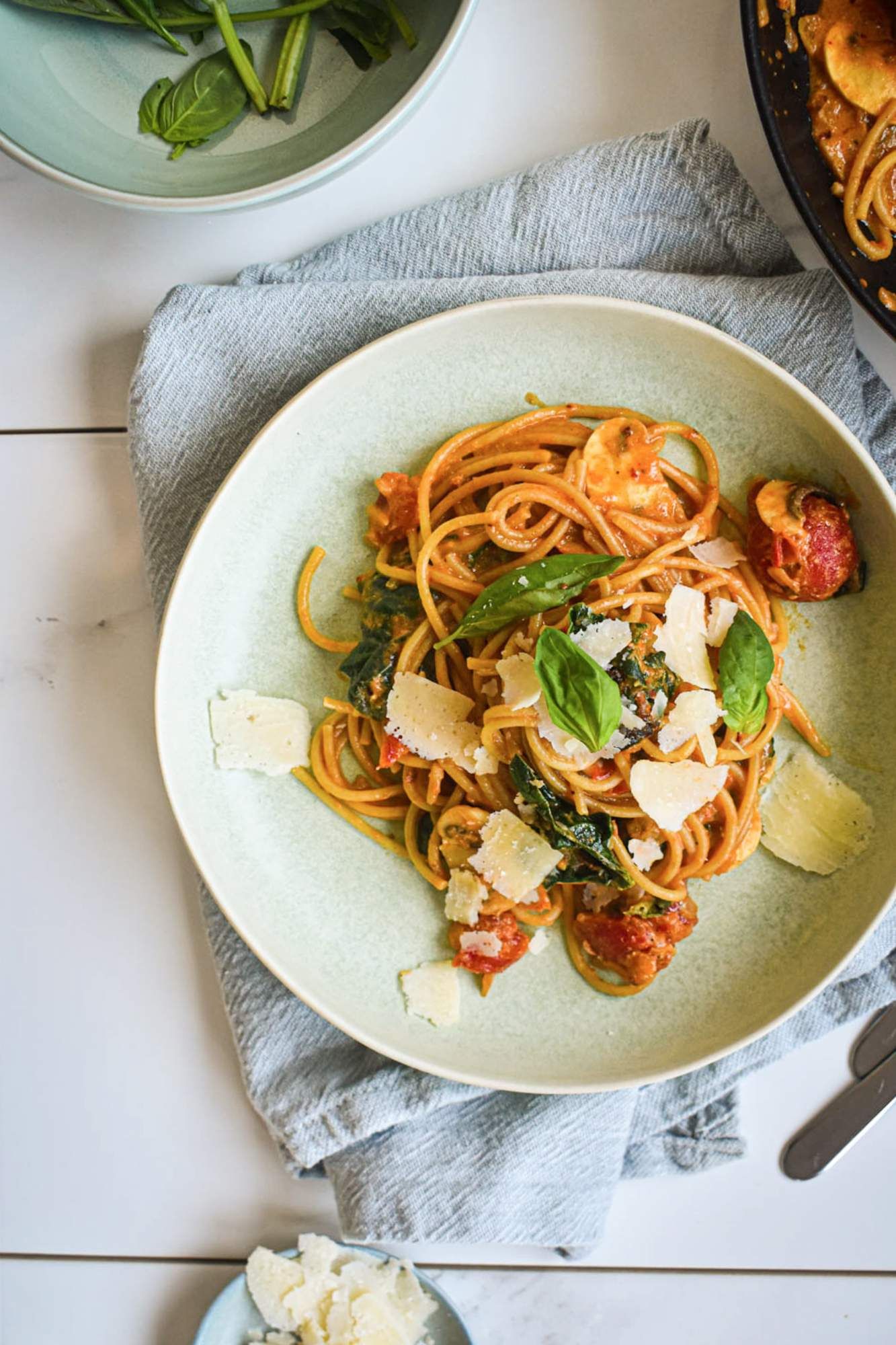 Pasta with spinach, tomatoes, mushrooms, and a creamy tomato sauce on a plate with Parmesan cheese and basil.