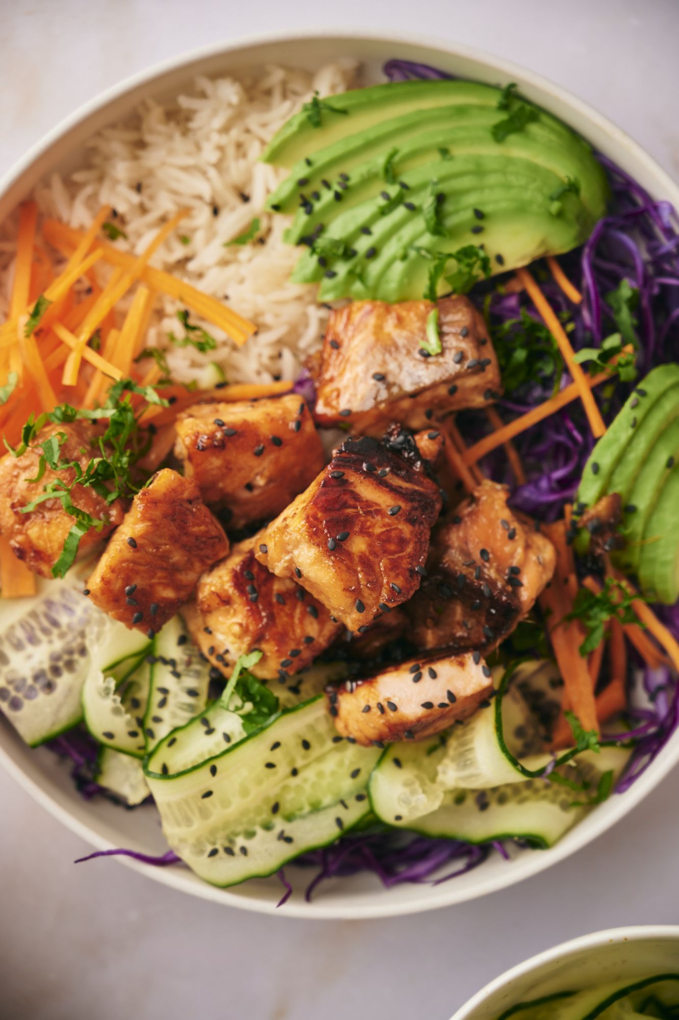 Asian salmon bowl with white rice, avocado, cabbage, cucumber, cilantro, and sesame seeds.