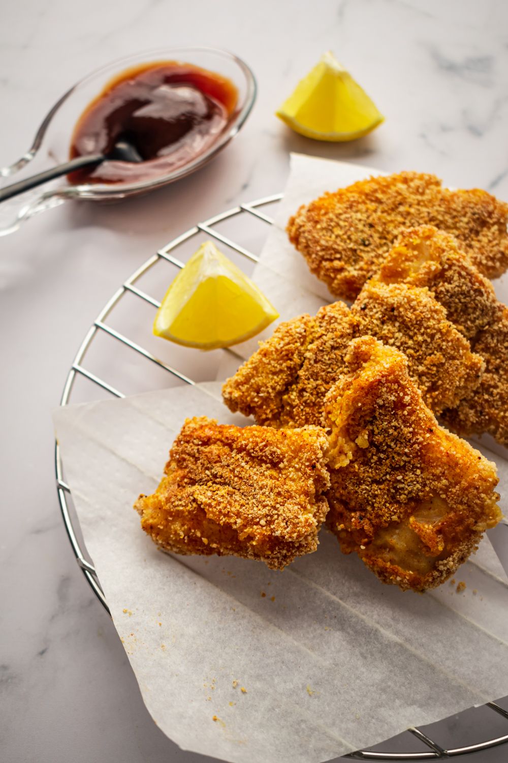 Baked breaded fish with a crispy coating on a wire rack with fresh lemon and dipping sauce.