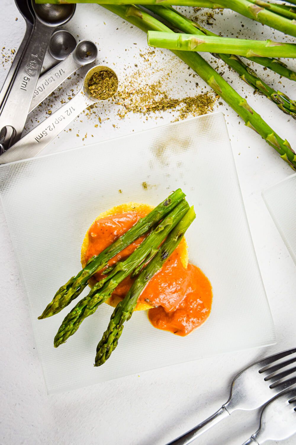 Polenta with asparagus spears and a creamy red sauce on a plate with dried herbs.