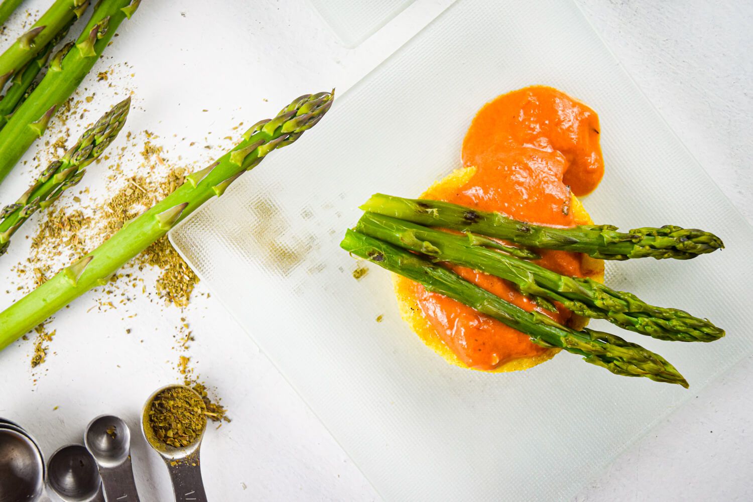 Asparagus, polenta, and a creamy tomato sauce on a glass dish with dried herbs.