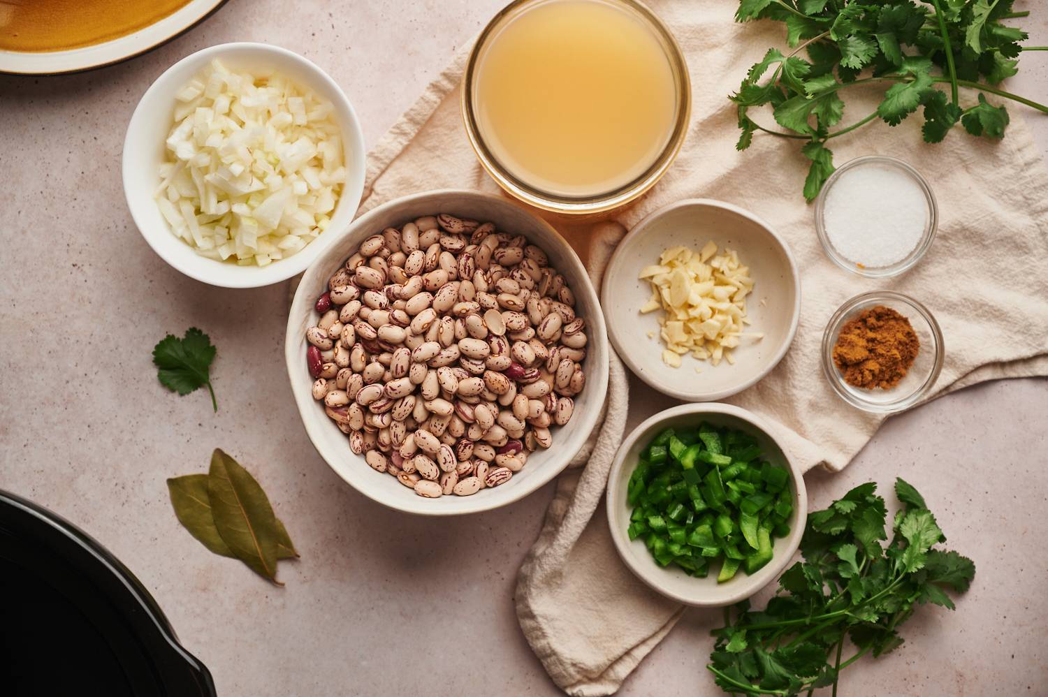 Ingrdients for slow cooker pinto beans including dried pinto beans, onion, garlic, pepper, cumin, salt, and broth.