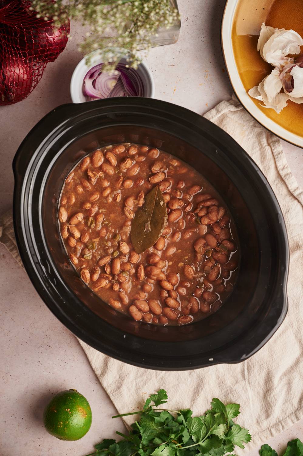 Slow cooker pinto beans with onions, peppers, and a bay leaf in a black crockpot.