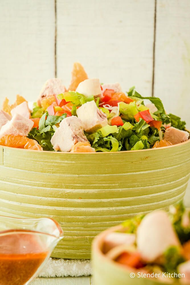 Thai Salad with chicken breast, cilantro, red pepper, mandarins, and peanut dressing in a green bowl.