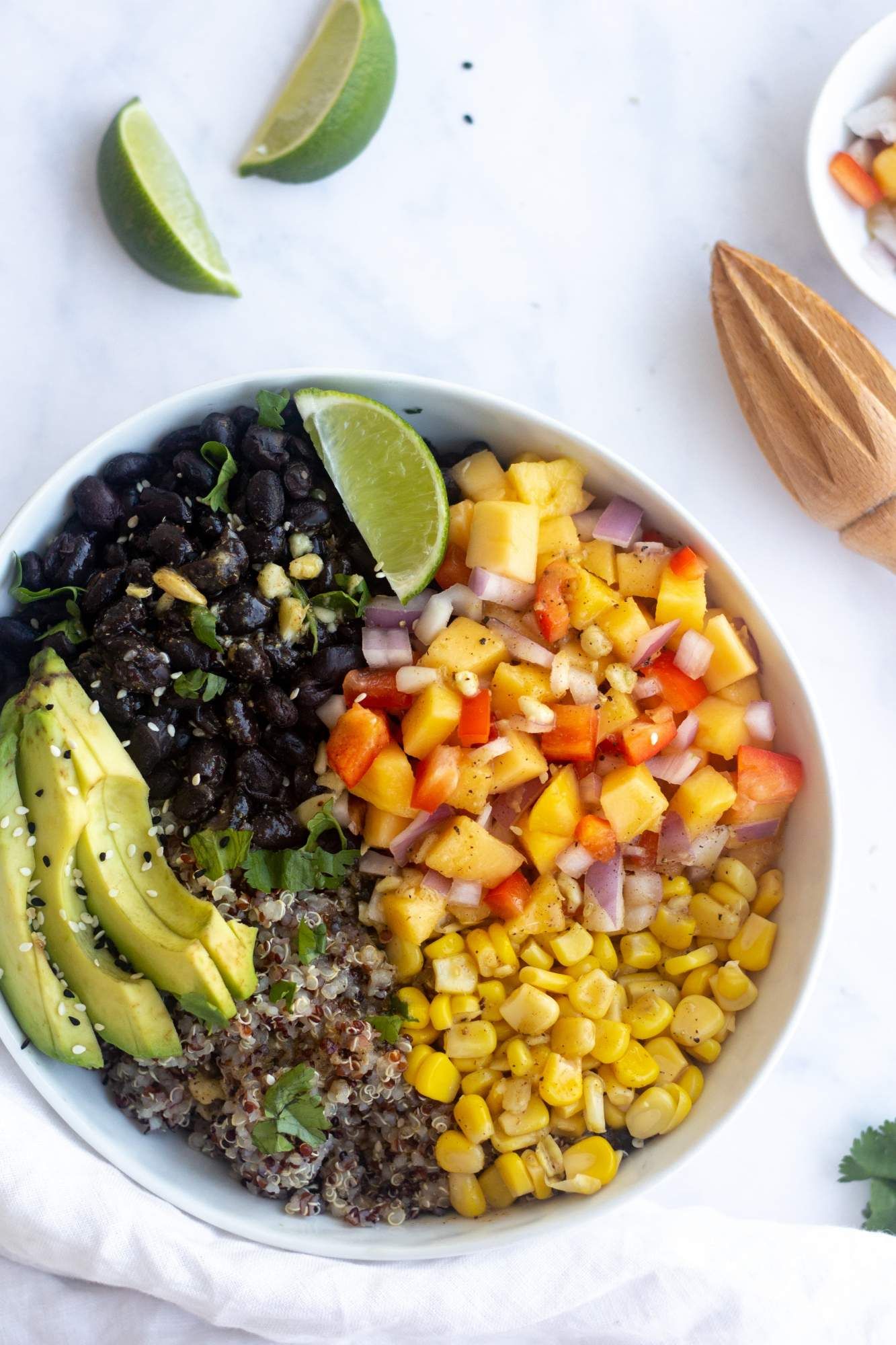 Black bean bowls with mango salsa, quinoa, black beans, and corn in a bowl with avocado and limes on the side.