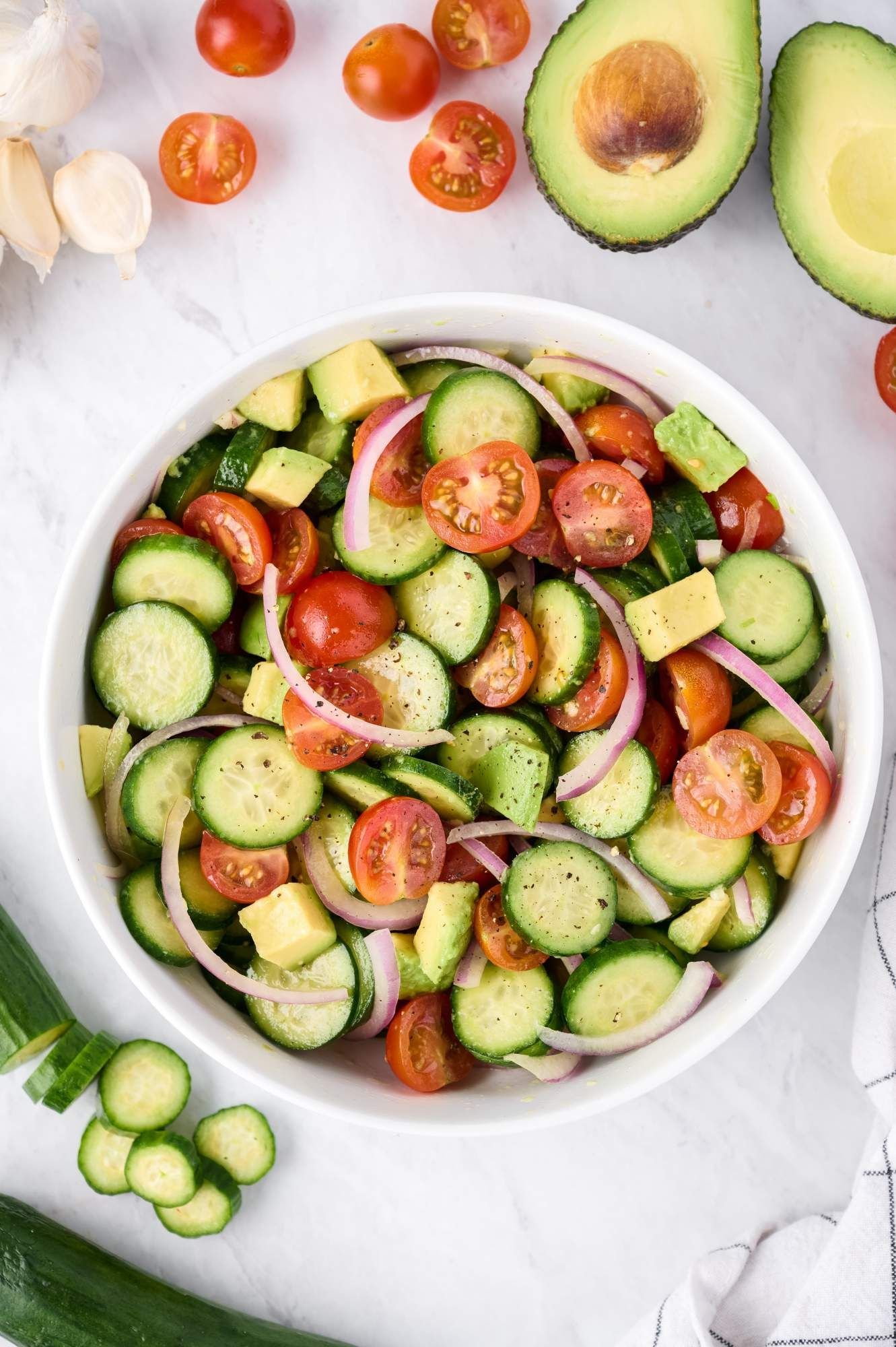 Cucumber and tomato salad in a bowl with avocado, onions, and white balsamic vinaigrette.