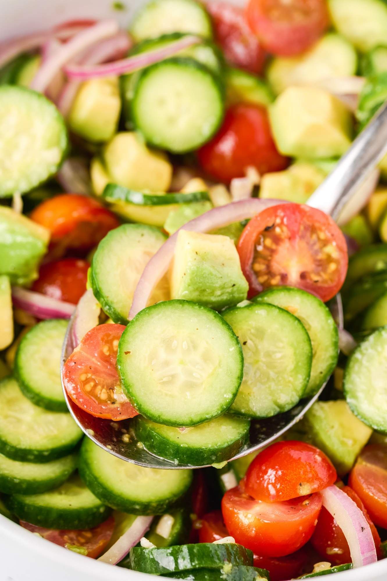 Spoonful of cucumber salad with avocado, tomatoes, red onions, olive oil, and garlic.