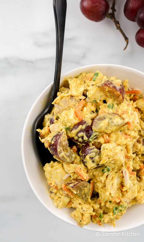 Curry chicken salad in a bowl with grapes, carrots, and green onions.