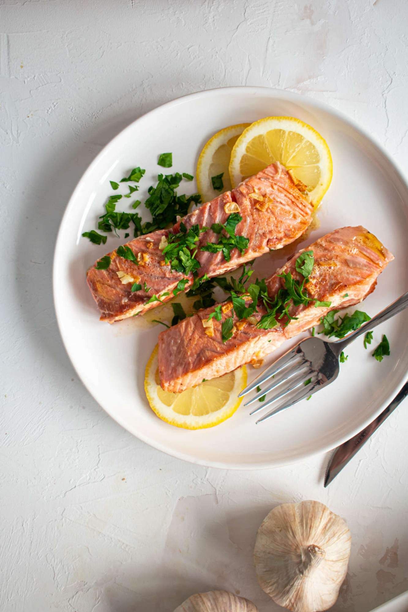 Baked salmon with fresh parsley, lemon slices, and a garlic Dijon sauce on a white plate.