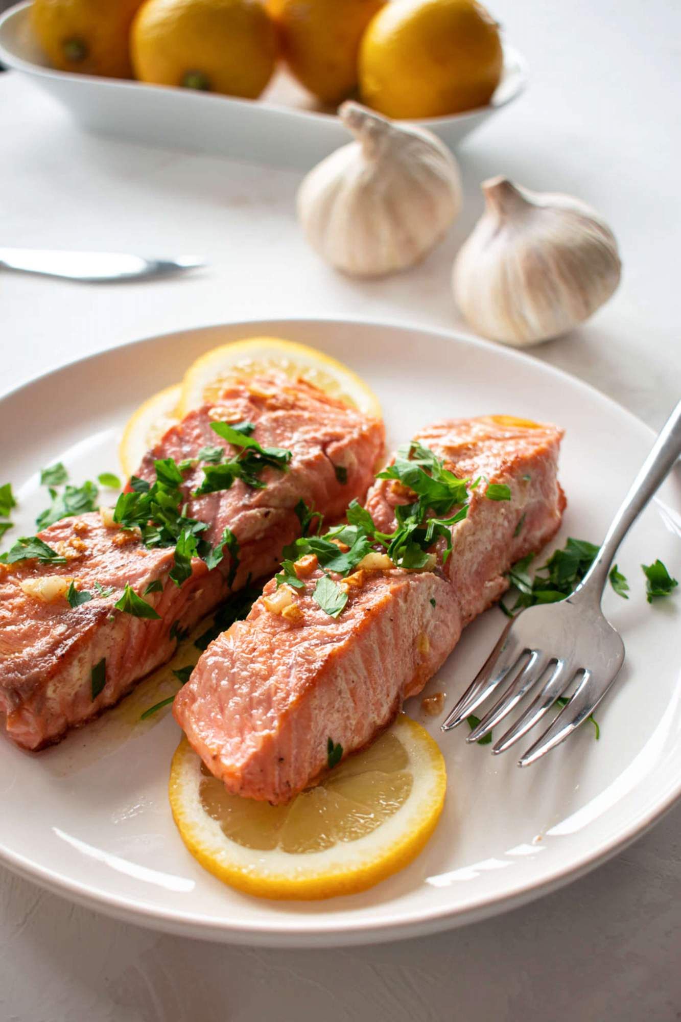 Baked salmon with lemon Dijon sauce on a plate with sliced lemons and parsley.