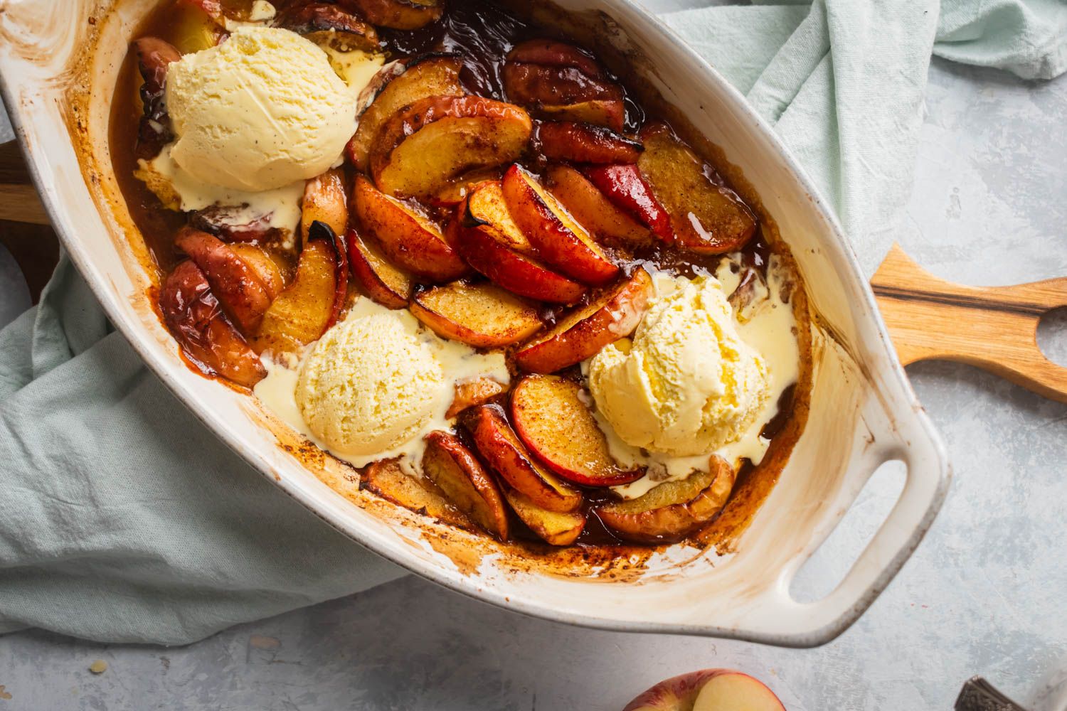 Apples baked with cinnamon and sugar with vanilla ice cream scooped on top in a baking dish.