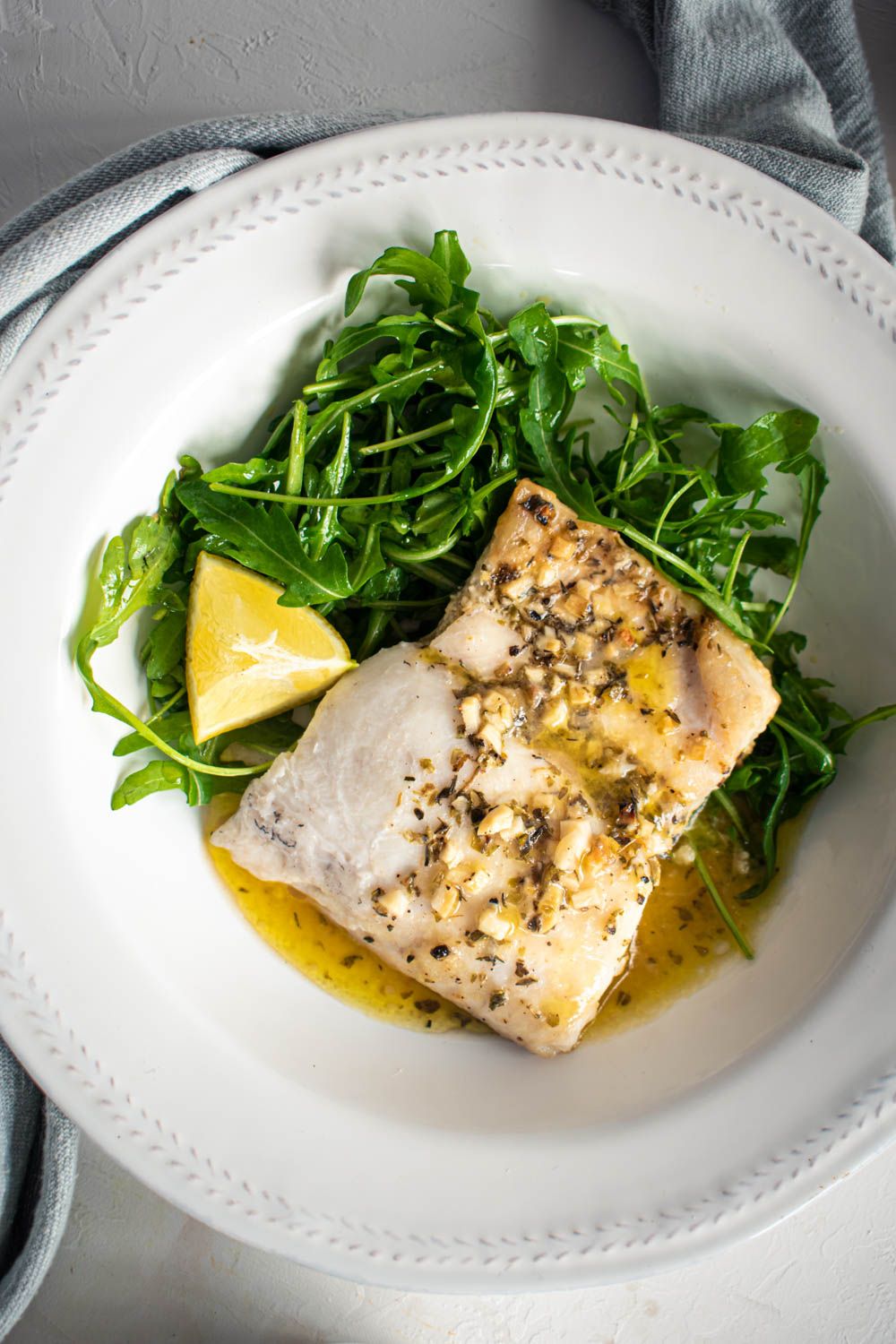 Cod baked with butter, garlic, and Italian seasoning on a plate with mixed greens.