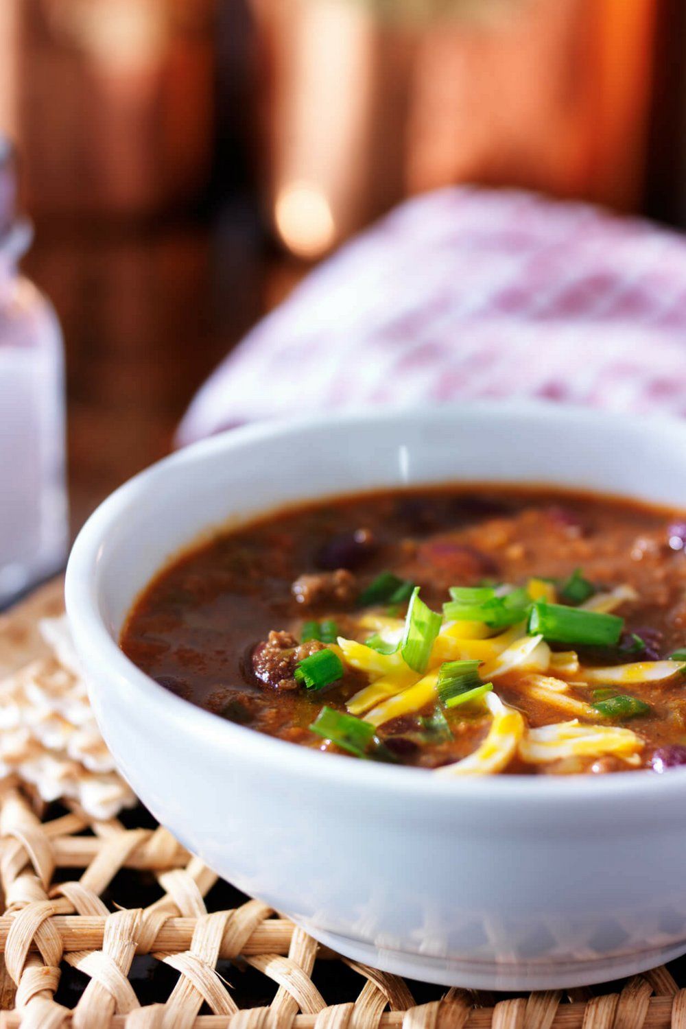 Beef chili in a white bowl with a glass blurred in the background.