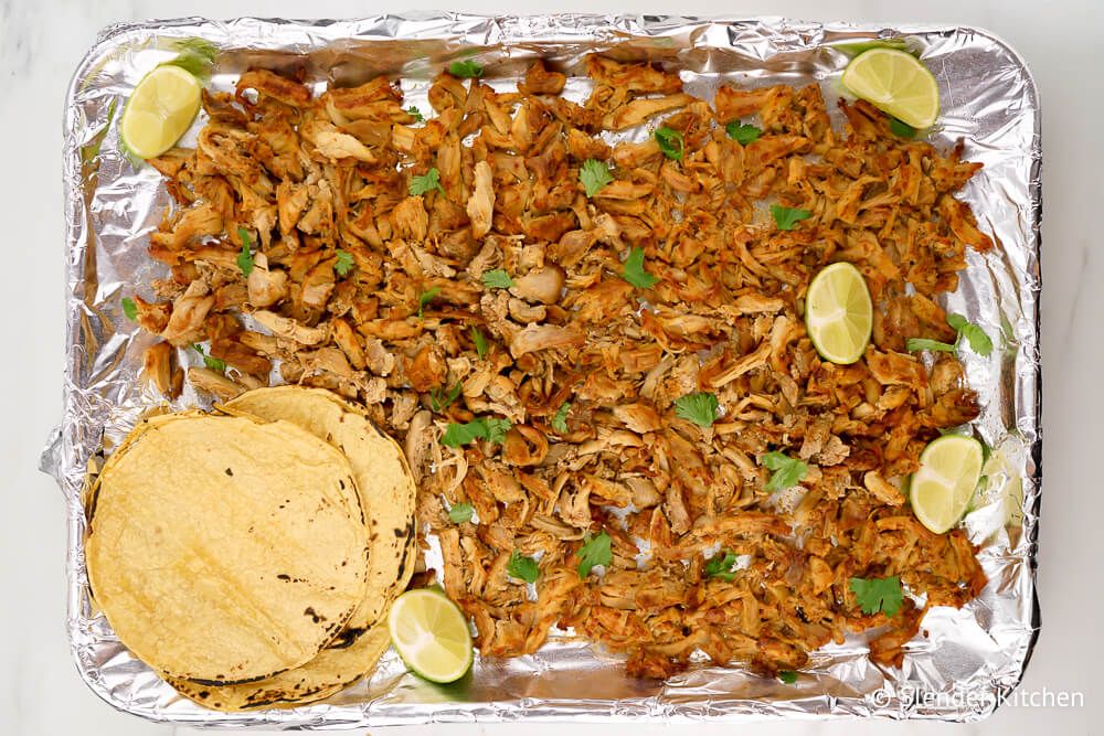 Instant Pot Carnitas on a baking sheet with tortillas and lime.