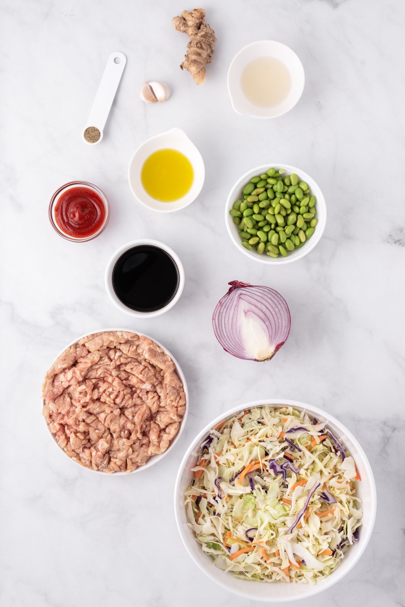 Ingredients for egg roll in a bowl including ground chicken, cabbage, carrots, ginger, garlic, oil, and soy sauce.