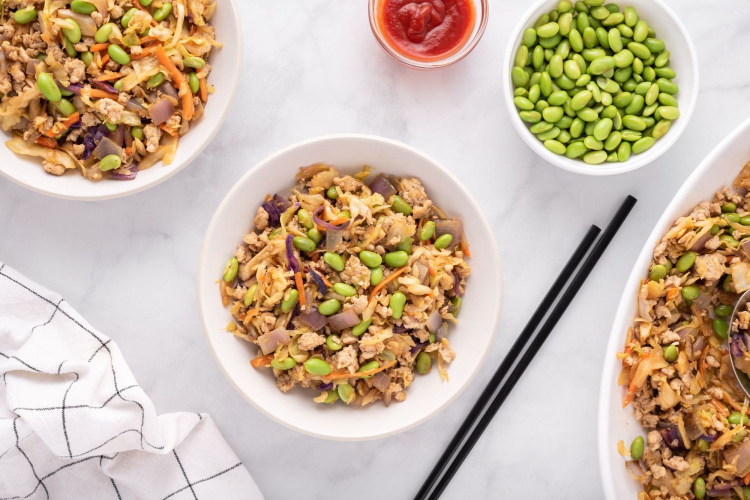 Three servings of egg roll bowls served with edamame, cabbage, carrots, and ground chicken. 