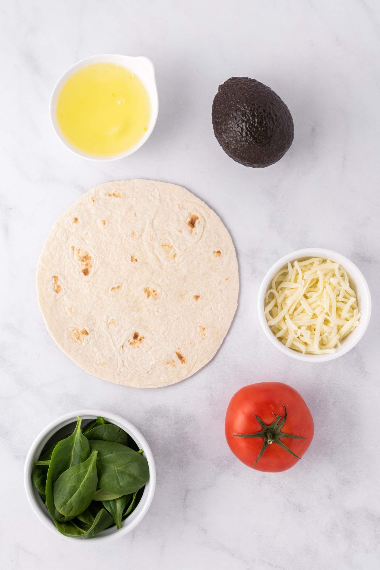 Ingredients for an egg white breakfast wrap including avocado, egg white, tomato, cheese, and spinach.