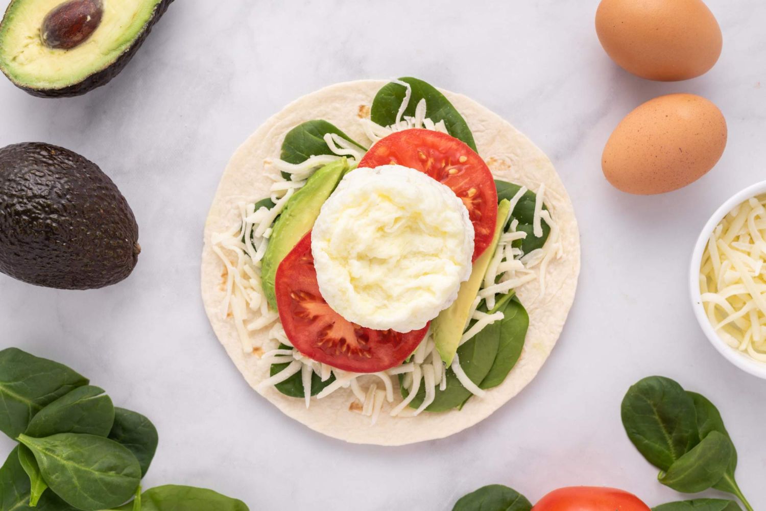 Breakfast egg white, tomato, and avocado on a tortilla with cheese and spinach.