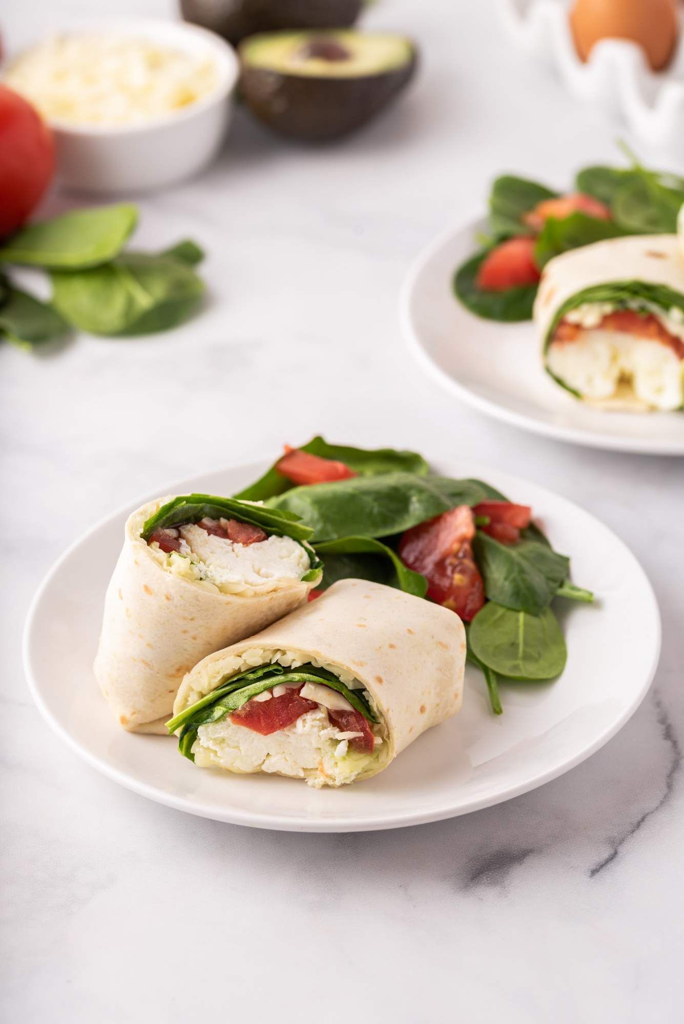 Egg white and avocado breakfast wrap on a plate with tomatoes and spinach.