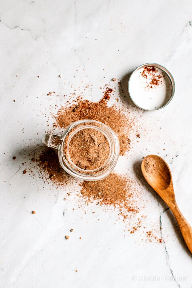 Fajita spices mixed in a small glass jar and some of the side on a wooden spoon.