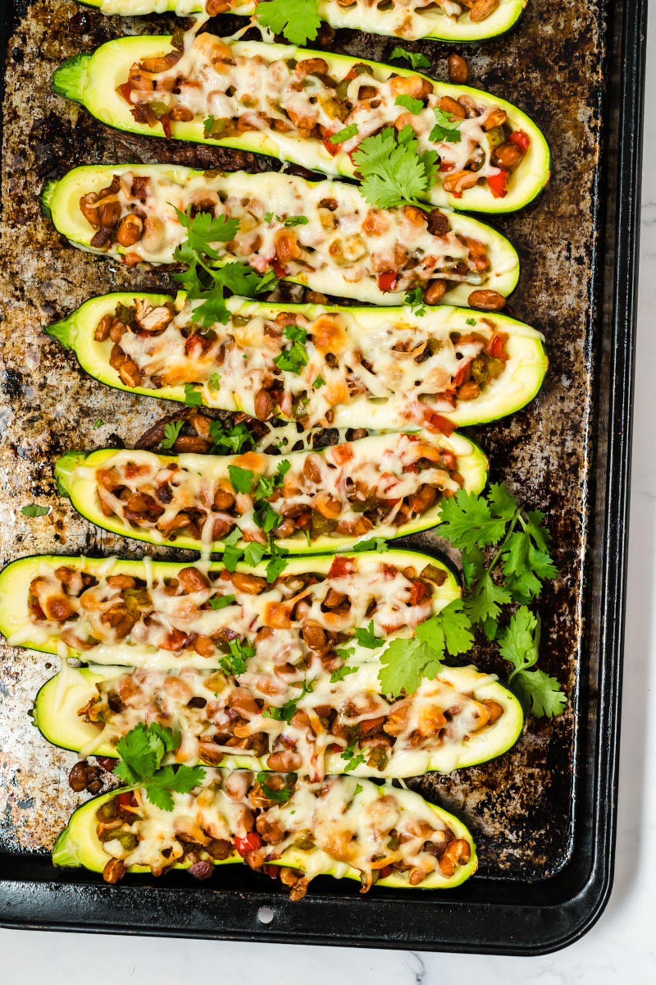 Pinto bean zucchini boats with peppers, onions, fajita seasoning, and melted cheese on a baking sheet.