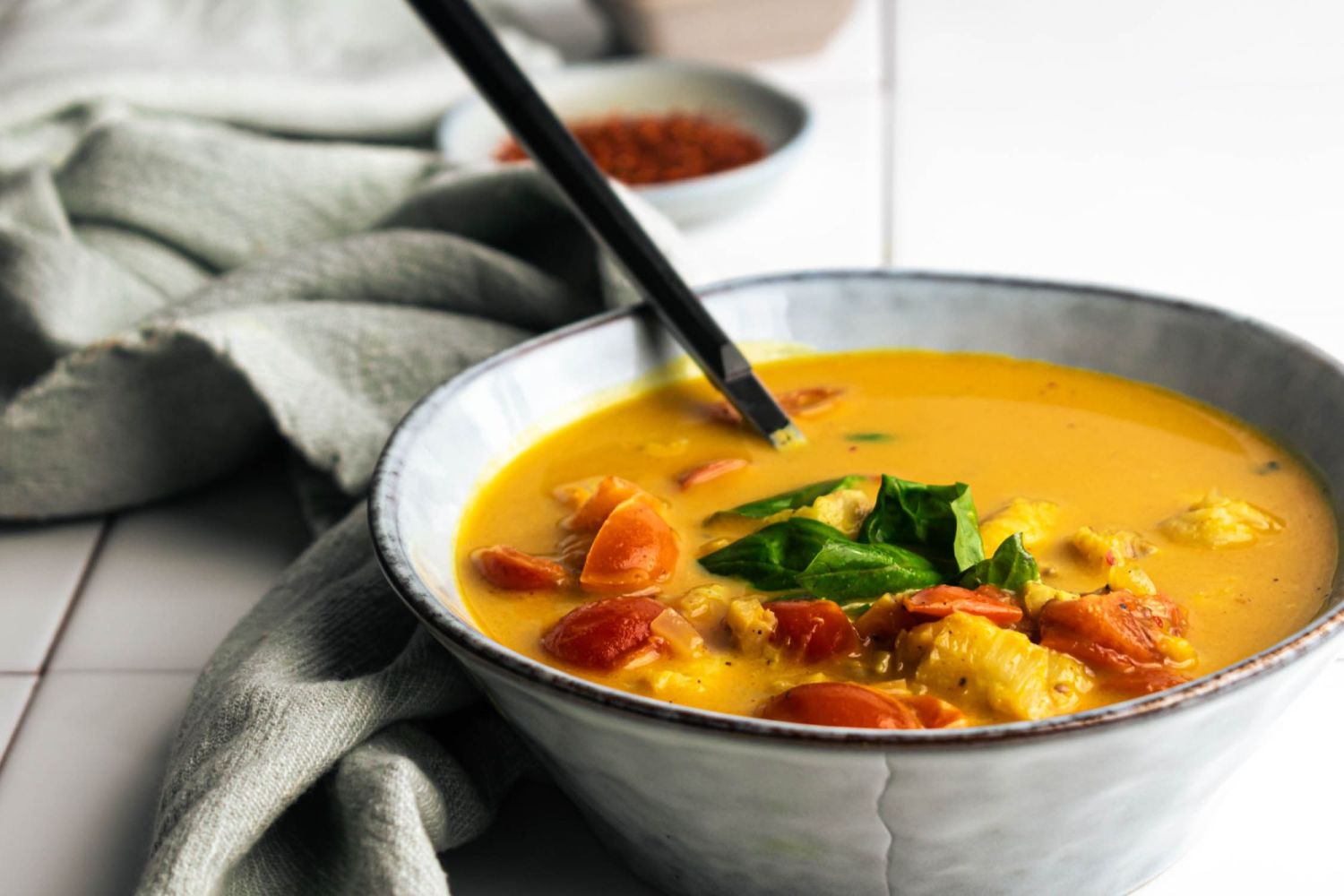 Curried fish in a bowl with a creamy coconut broth, cherry tomatoes, and fresh basil in a bowl.