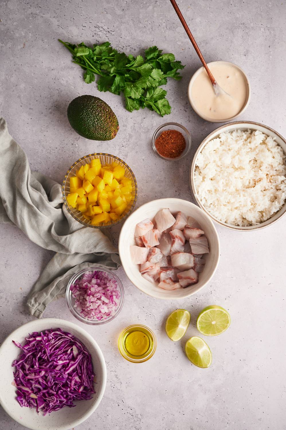 Ingredients for fish taco bowls including mahi mahi, mango, cabbage, cilantro, red onion, rice, lime juice, and spices. 