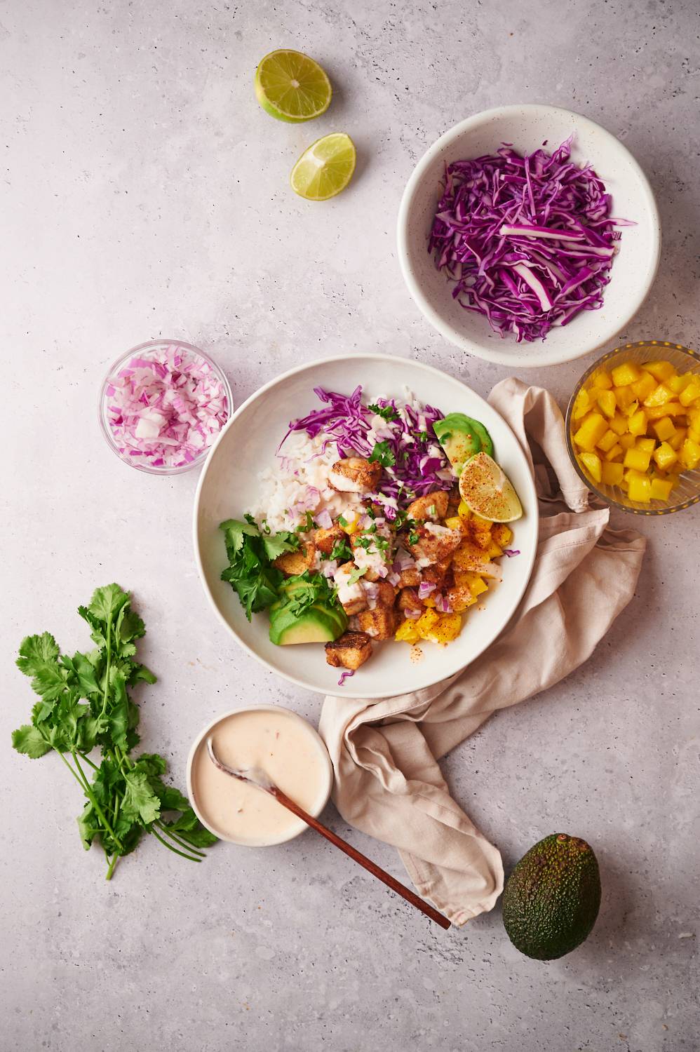 Blackened fish taco bowsl with flaky fish, mango salsa, red shredded cabbage, avocado, and limes with fish taco sauce on the side.