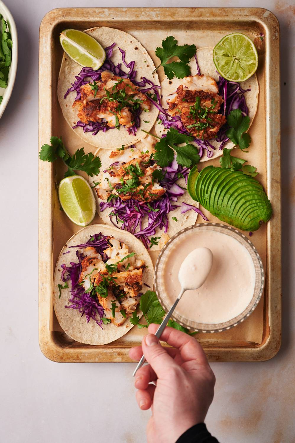 White fish taco sauce served with seasoned fish, cabbage, cilantro, and avocado in corn tortillas.