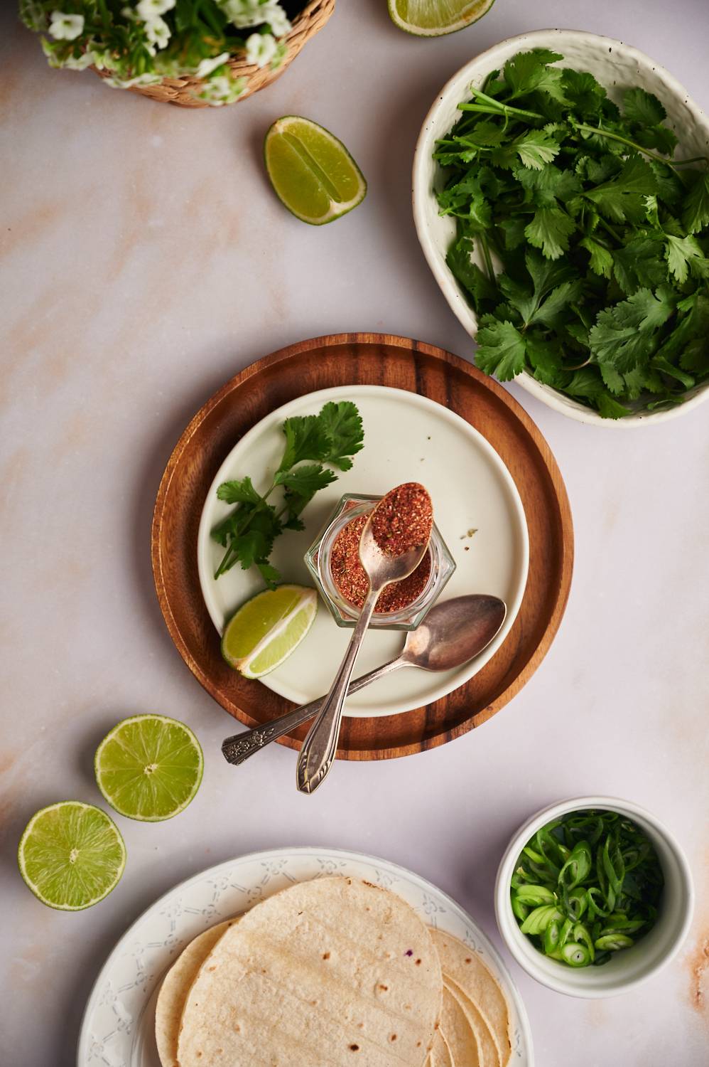 Fish taco spice rub with chili powder, paprika, garlic powder, onion powder, salt, and pepper in a jar with cilantro, limes, and tortillas on the side.