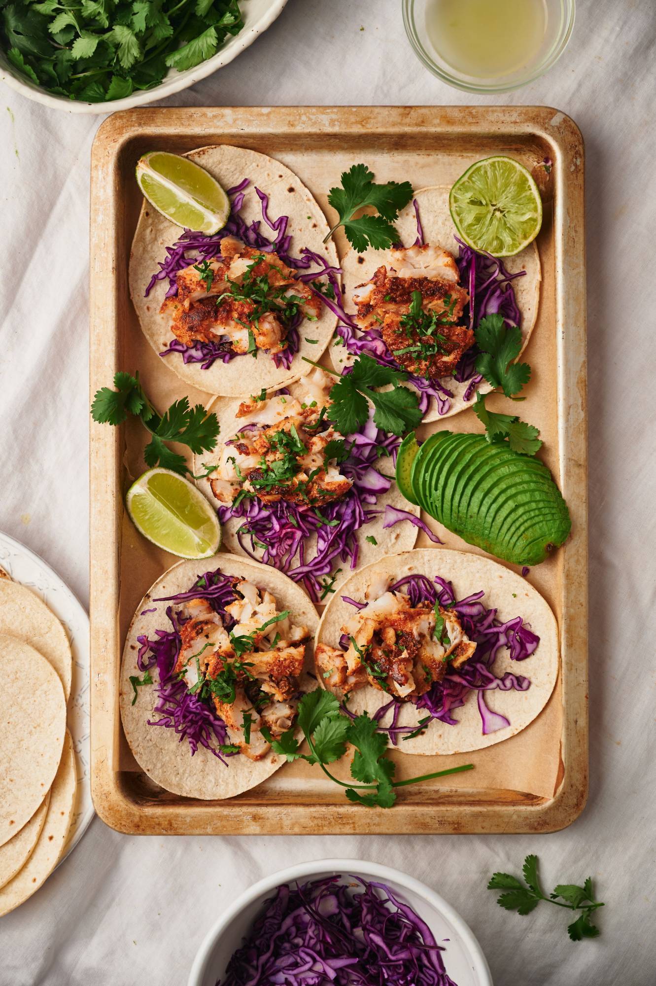 Cod fish tacos with shredded red cabbage, cilantro, and avocado served with lime wedges. 