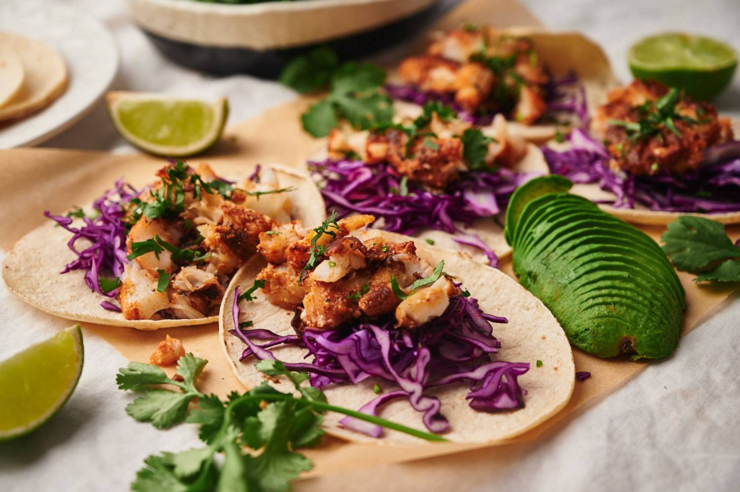 Mexican fish tacos served on warm corn tortillas with slaw, avocado, and lime wedges.