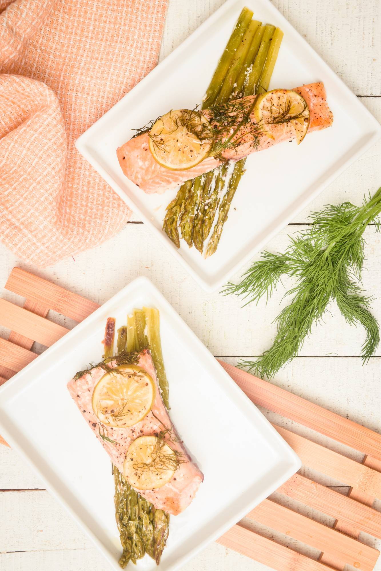 Baked salmon with asparagus on two plates served with fresh dill and lemon.