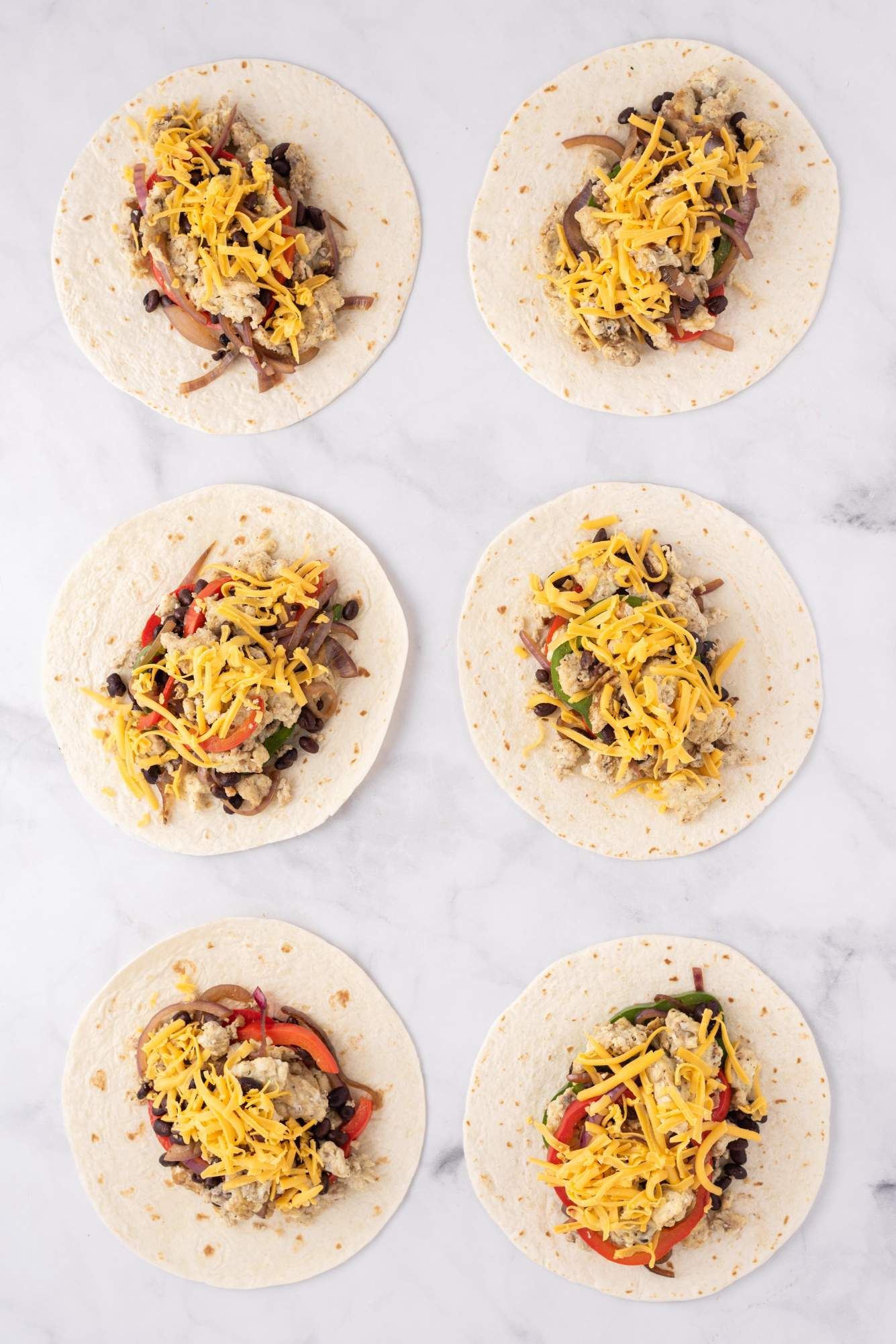 Freezer breakfast burritos ready for the freezer with tortillas, eggs, cheese, black beans, and peppers.