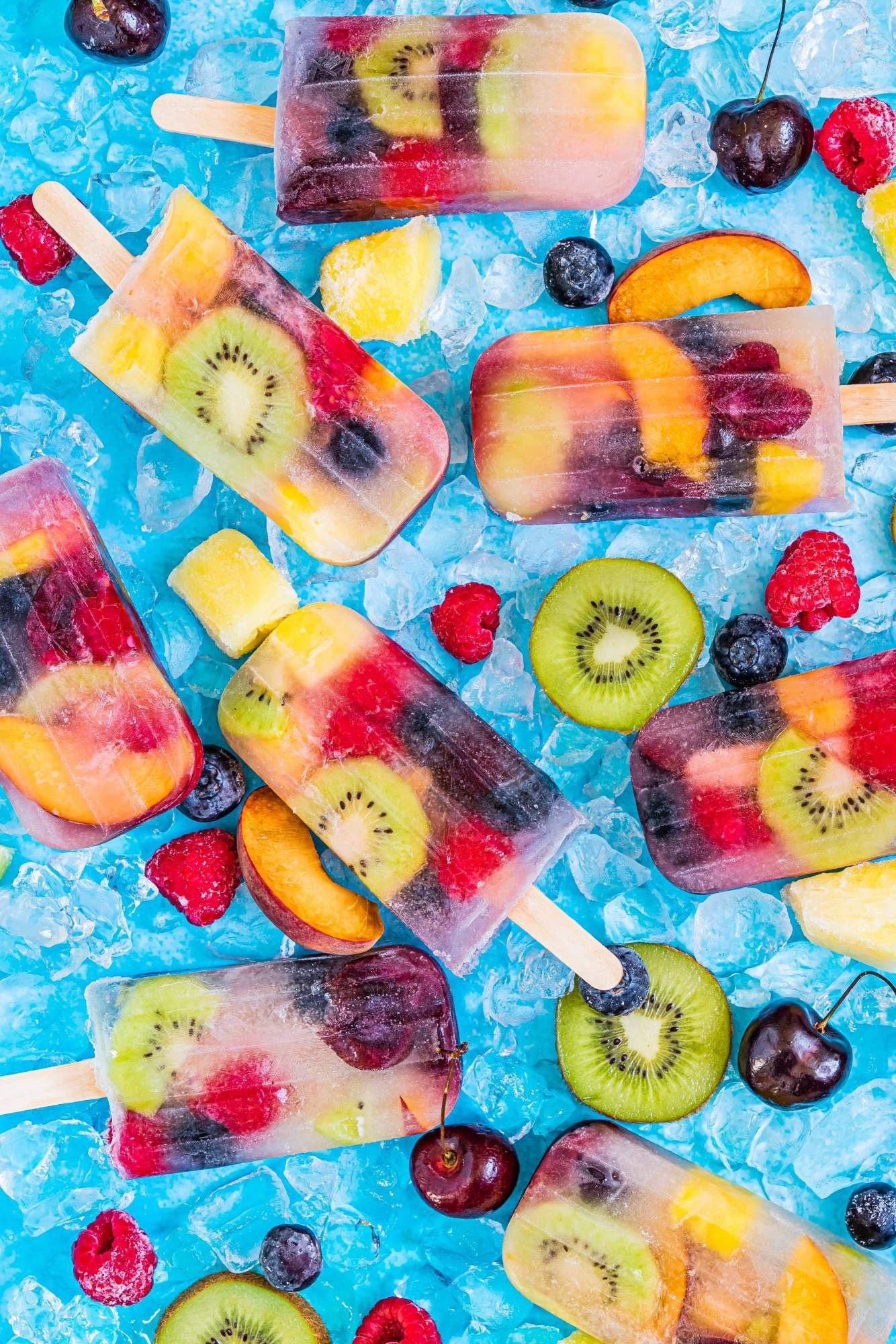 Homemade coconut and fruit popsicles with cherries, pineapple, peaches, and berries on the side.