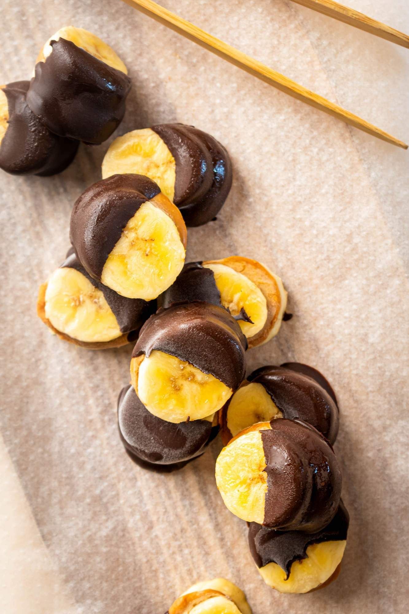 Frozen chocolate banana sandwiches with peanut butter on a wooden board.