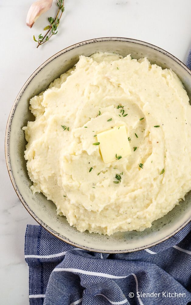 Garlic cauliflower mashed potatoes in a bowl with garlic and thyme on the side.