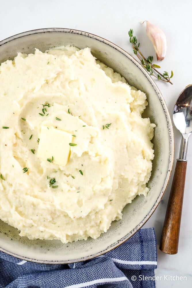 Mashed cauliflower and potatoes in a bowl with a pat or butter, fresh thyme, and a spoon.